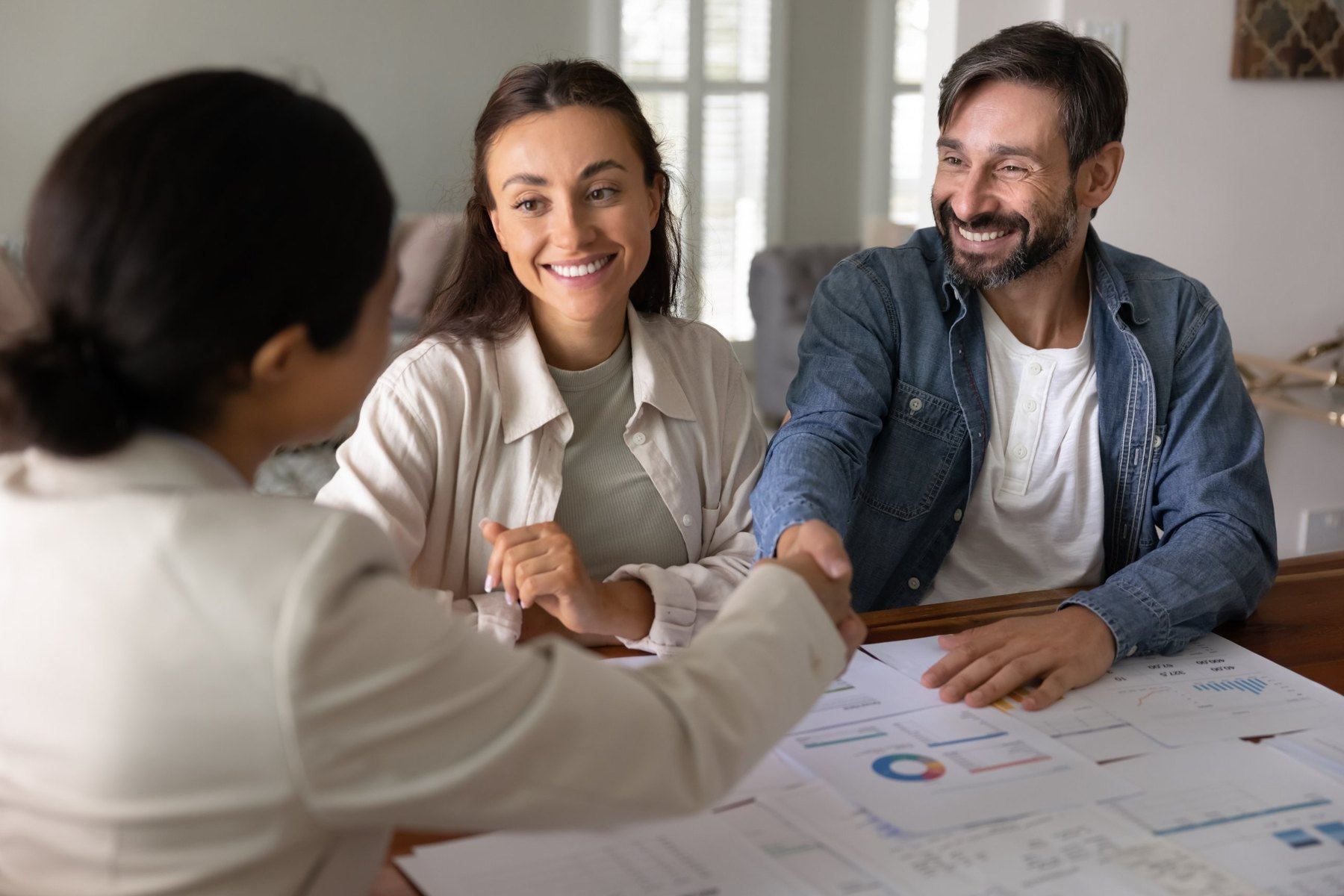 A couple shaking hands with their advisor across a table covered in financial reports